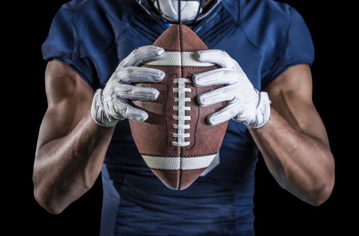 Close up view of an American Football player holding a football with receiver gloves. GLOVE DOVE® The Ultimate Glove Saver!™ can be used for your football gloves